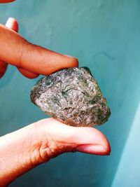 Cropped hand holding precious gem against turquoise wall