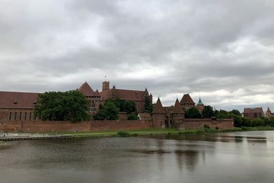 Buildings by river against sky