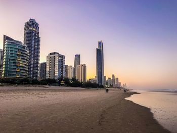 Sea and modern buildings against sky during sunset