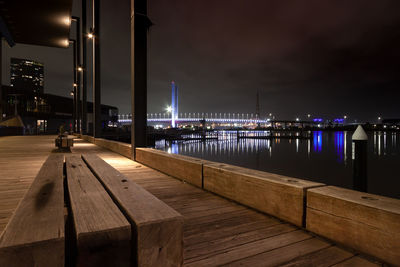 Illuminated pier over river against sky at night