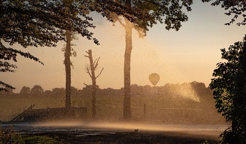 Silhouette of agricultural irrigation system watering cornfield at sunset.