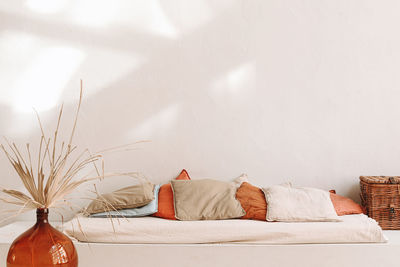 A glass vase with dried flowers next to a bed with natural materials, minimalist aesthetic