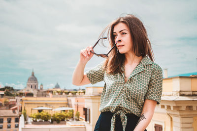 Portrait of young smiling woman in sunglasses on a rooftop with a panoramic view of rome, italy