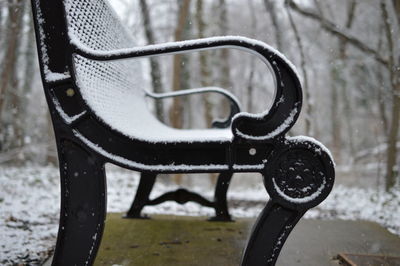 Close-up of snow covered bench at park during winter