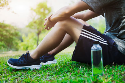 Low section of man sitting on grassy field with water bottle