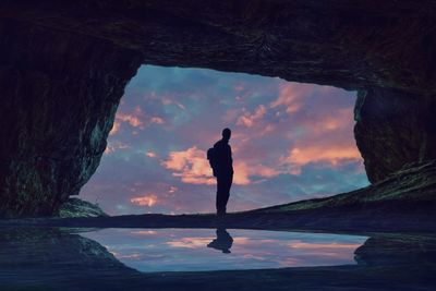 Silhouette man standing in cave by sea against sky