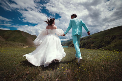 Wedding couple runs. happy man and woman running through a field in the mountains after a wedding