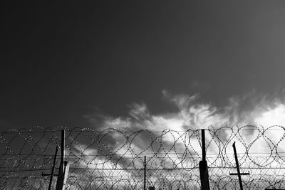 Barbed wire fence against cloudy sky