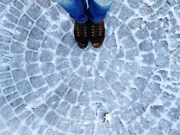 Low section of person standing on snow covered cobblestone