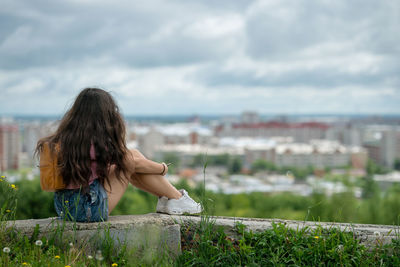 A tourist girl in a pink t-shirt with an orange backpack is sitting and enjoying panoramic view.