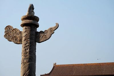 Low angle view of carvings on architectural column against clear blue sky