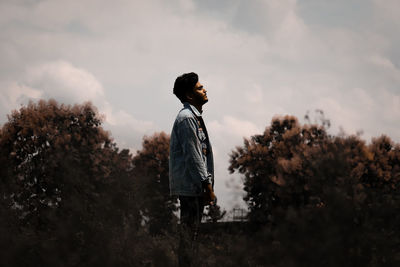 Side view of boy standing on field against sky