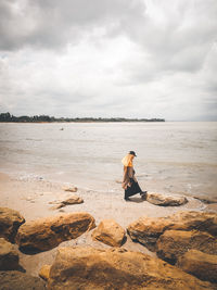 Man sitting on shore at beach against sky