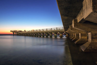 Low angle view of pier over sea against clear blue sky at dusk