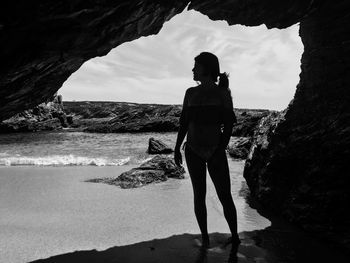 Woman standing on rock by sea against sky