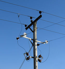 Low angle view of electricity pylon against clear blue sky