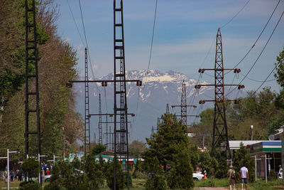 Electricity pylons by trees against sky