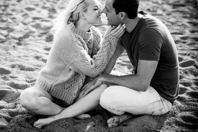 Young couple kissing while sitting at beach