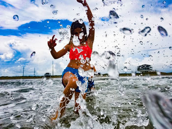 Cheerful woman playing in lake against sky seen through wet glass