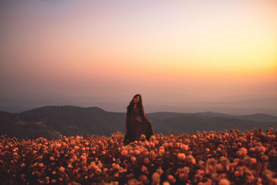Beautiful woman standing amidst field against sky during sunset