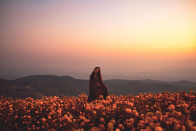 Woman standing on field against sky during sunset