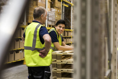 Smiling young worker looking at senior coworker standing at distribution warehouse