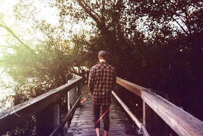 Rear view of man walking on wooden bridge on sunny day