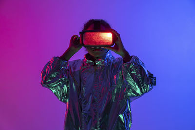 Woman wearing virtual reality simulator standing against multi-colored background