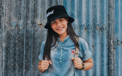 Portrait of smiling young woman standing against wall