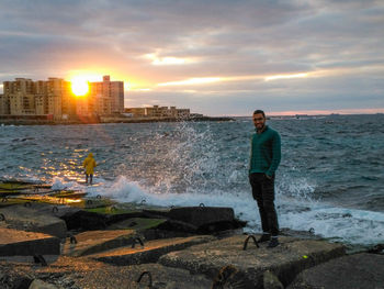 Man standing on rock by sea against sky during sunset