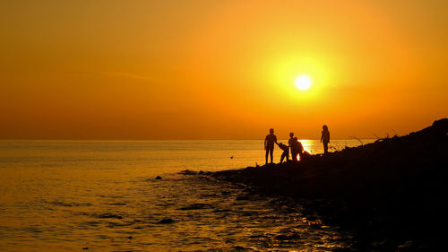 Silhouette people on beach against sky during sunset