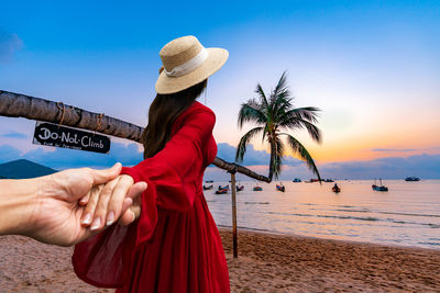 Midsection of woman holding umbrella at beach against sky