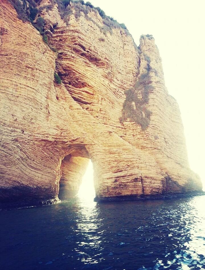 water, rock formation, rock - object, sea, waterfront, tranquility, scenics, beauty in nature, tranquil scene, nature, cliff, cave, clear sky, geology, sky, idyllic, sunlight, rock, reflection, rippled