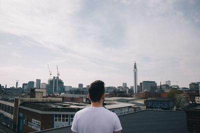 Rear view of man looking at city buildings against sky