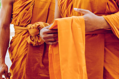 Midsection of monks holding fabric while standing outdoors
