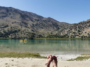 Low section of person relaxing in lake against sky