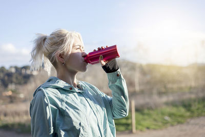 Woman drinking water while standing on field against sky