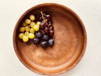 Plums and grapes in  wooden bowl. two bunches. red grapes, green grapes. purplish blue plums. 