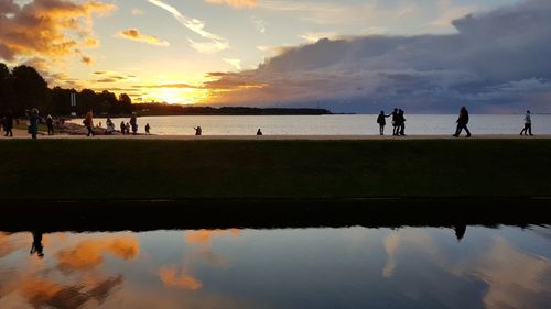 Silhouette people on beach against sky during sunset