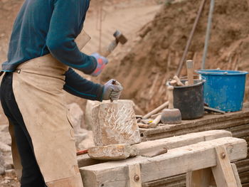 Midsection of craftsperson using hammer and chisel on rock