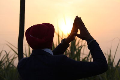Rear view of man gesturing while standing against sky during sunset