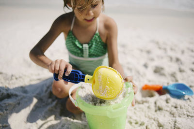 Girl playing with sand pail and shovel at beach during sunny day