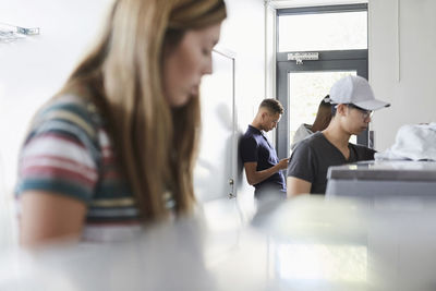 Man using phone while university friends working at laundromat