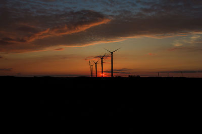 Silhouette of windmills on field against sky during sunset