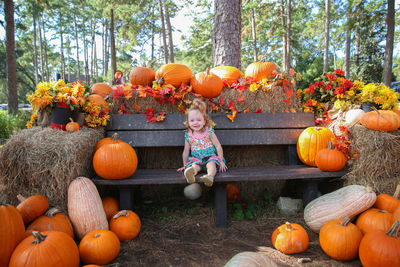 Girl sitting on bench amidst pumpkins at park during autumn