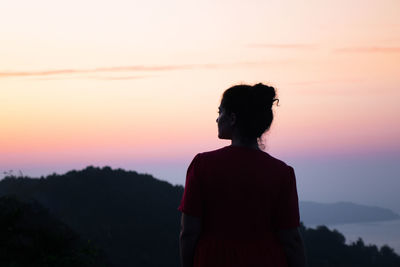 Rear view of silhouette woman standing against sky during sunset