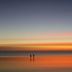 Silhouette people standing on sea against sky during sunset
