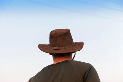 Back view of a young shirtless man wearing a cowboy hat. young cowboy looking on blue sky away. 