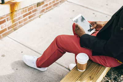 Man sitting in the street, using digital tablet, drinking coffee