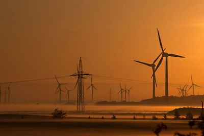 Silhouette windmills against sky during sunset